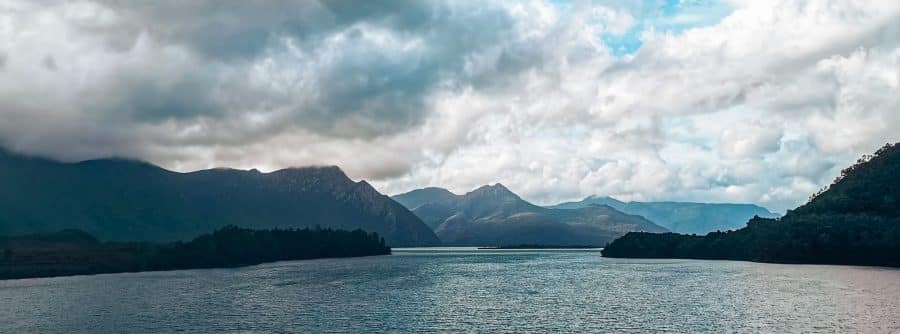 Dramatic mountains line calm peaceful waters next to the road driving around Tasmania, Australia