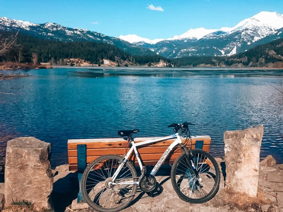 Helen's bike propped against a bench overlooking Green Lake with snow-capped mountains in the distance, Whistler in summer, British Columbia, Canada