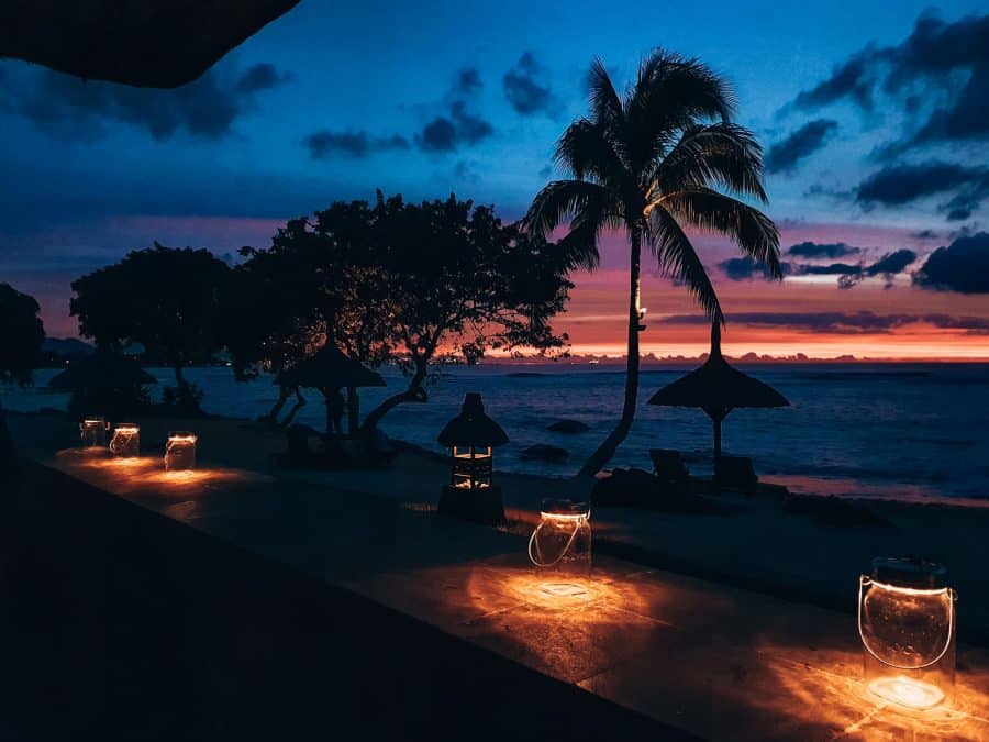 A beautiful sunset of pinks, oranges and reds over the Indian Ocean with silhouettes of palm trees at The Oberoi Mauritius