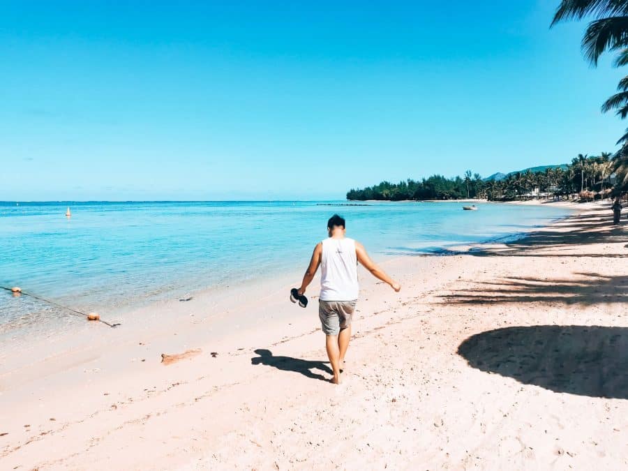 Andy walking down the picture-perfect white-sand beach at The Heritage Awali, lined with palm trees, Bel Ombre, Mauritius