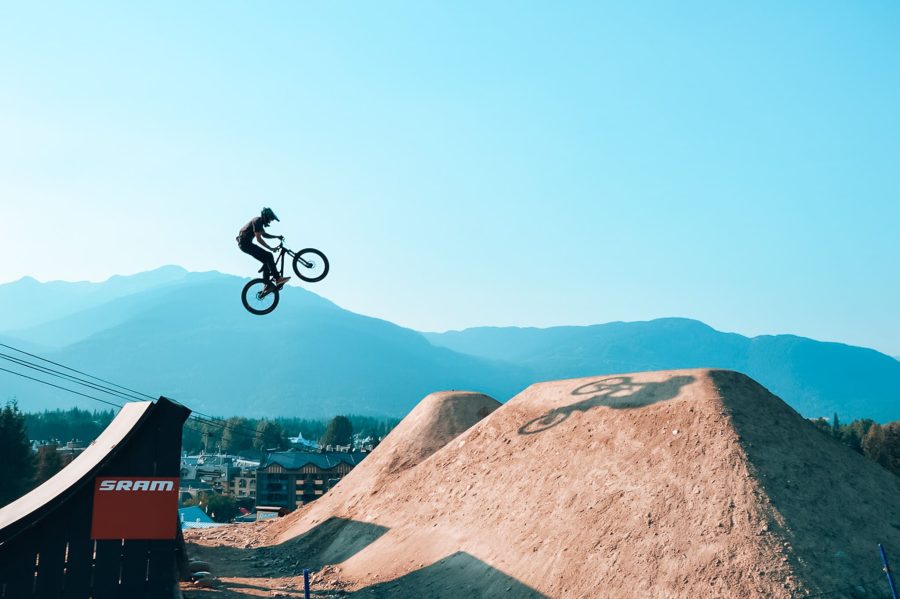 A biker jumping in Whistler Bike Park with mountains in the background, British Columbia, Canada