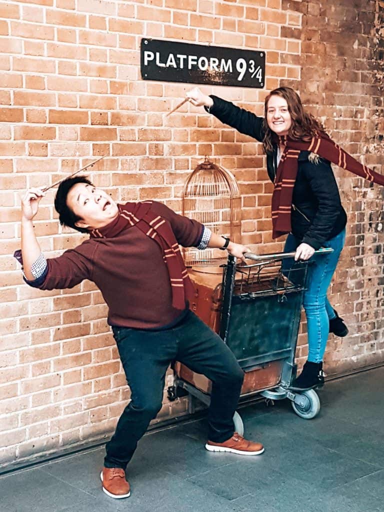 Andy and Helen pretending to jinx each other at the trolley in the wall at King's Cross Platform 9 3/4, London, England, UK