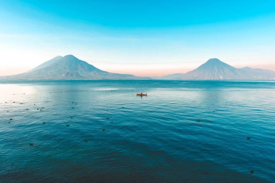 A solo kayaker on the calm water of Lake Atitlan with two volcanoes towering over then, Guatemala