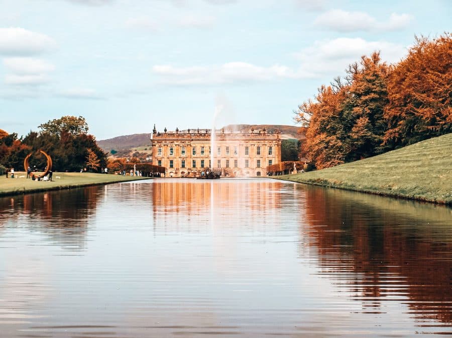 The grandiose Chatsworth House at the end of a large tranquil pond and fountain in the Peak District