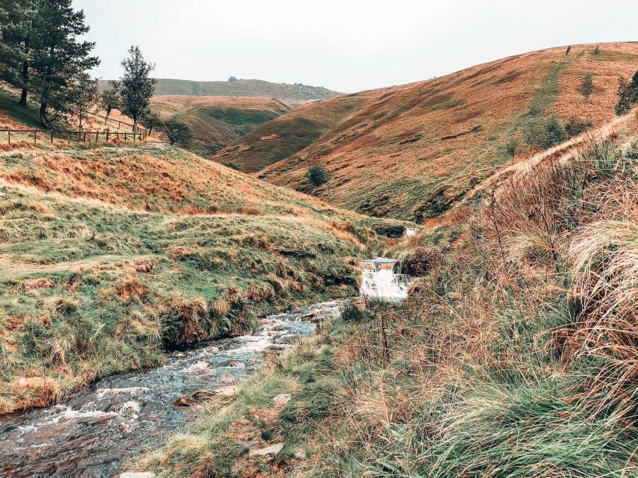 Rolling green hills with a picturesque stream flowing down the valley on the hike up Kinder Scout, one of the best things to do in the Peak District, Derbyshire