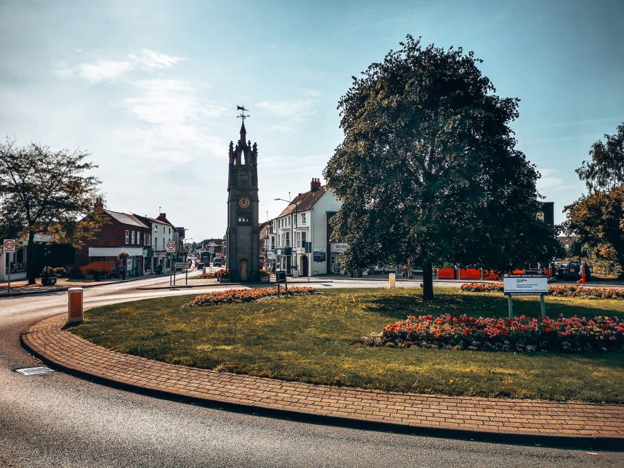 A roundabout with flowers and trees on in front of a clock tower on Warwick Road in Kenilworth, High Street