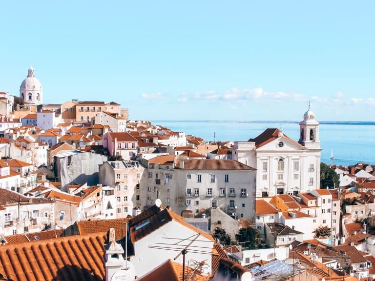 View over red roofs and white-washed houses out to the ocean from a viewpoint in Lisbon