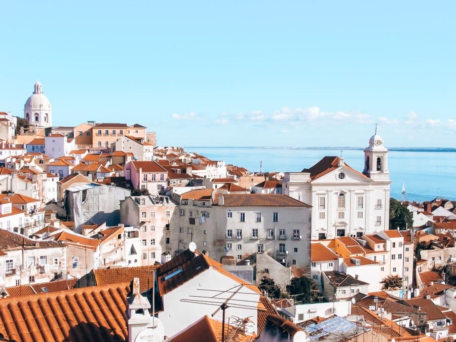 View over red roofs and white-washed houses out to the ocean from a viewpoint in Lisbon