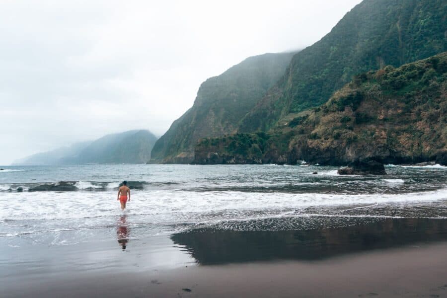 Andy walking into the sea with a dramatic mountain backdrop at Seixal Beach, Madeira, Portugal