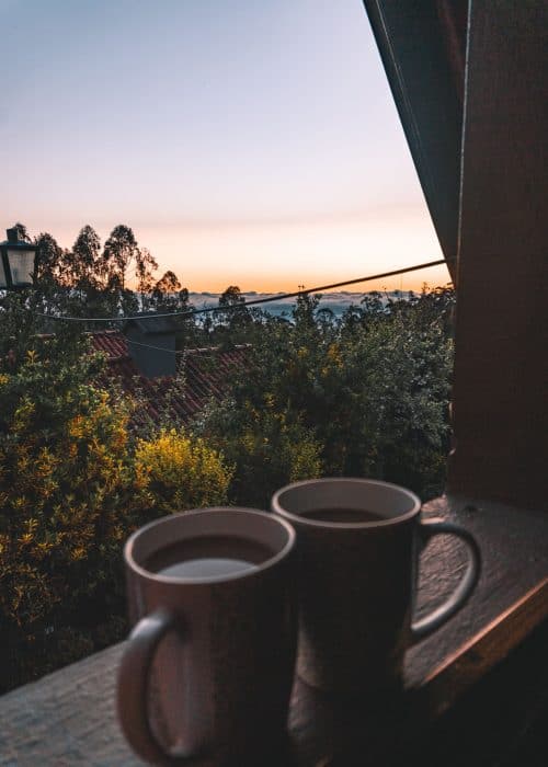 Cups of coffee on the windowsill of our traditional Santana House as we watch the sunrise light up the sky, Madeira, Portugal