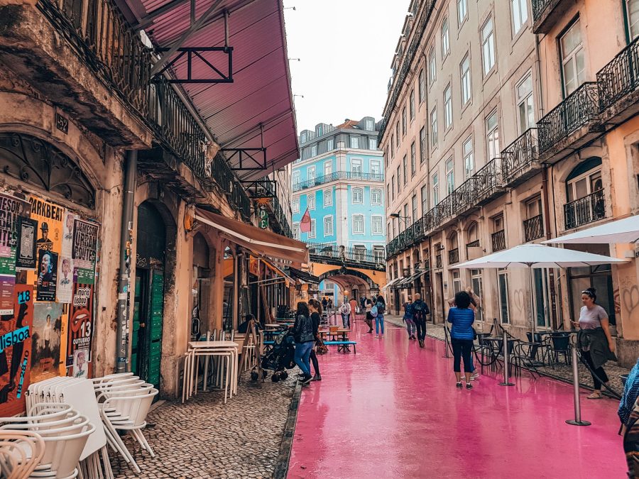 A bright pink street in between old yellow buildings in Bairro Alto, places you must see in Lisbon, Portugal