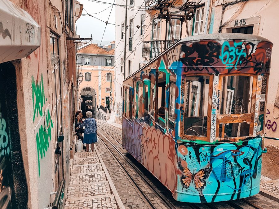 A yellow tram with vibrant street art on a steep cobbled street, Elevador da Bica, Lisbon, Portugal