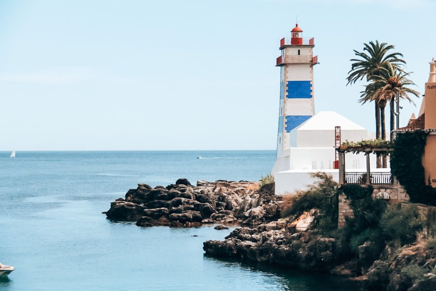 A pretty blue and white lighthouse at the edge of the ocean in Cascais, day trips from Lisbon by train