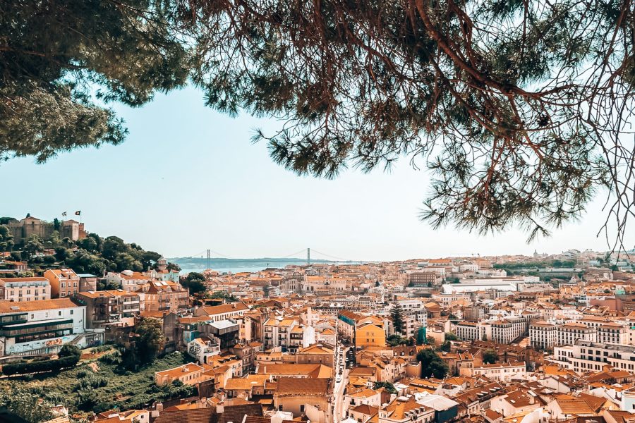 View from Miradouro da Graça across white-washed houses with red roofs out to the ocean, best viewpoints in Lisbon for sunset, Portugal