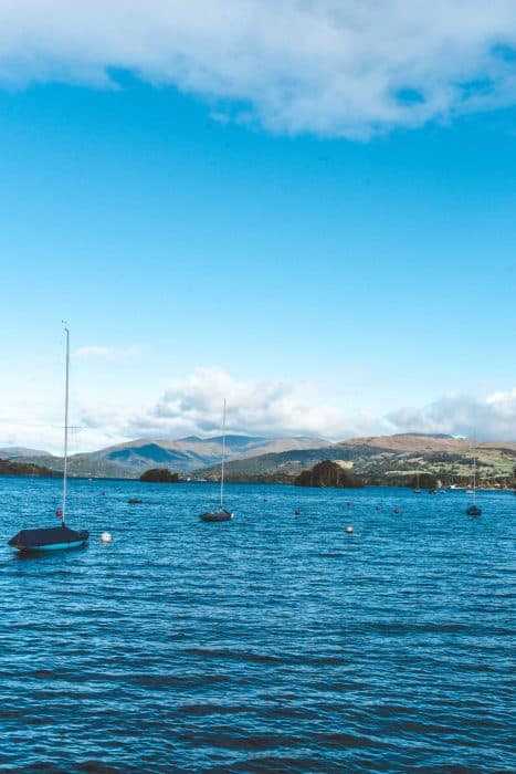 Boats floating on Lake Windermere with mountains towering in the distance, Lake District, Bowness, England, UK