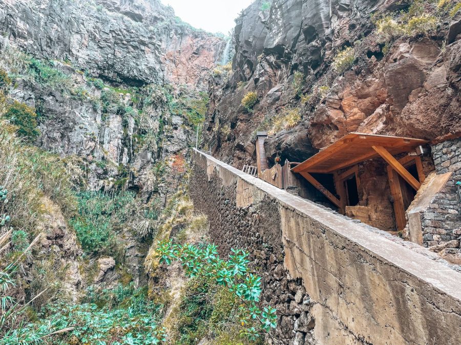 View from the bottom of the steps up to the waterfall hidden behind the gigantic volcanic cliff with ancient cave houses carved into it's side, Calhau da Lapa, Madeira, Portugal