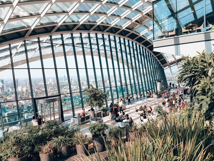 Inside the Sky Garden overlooking its cafe filled with plants and trees and out to the London skyline, England, UK