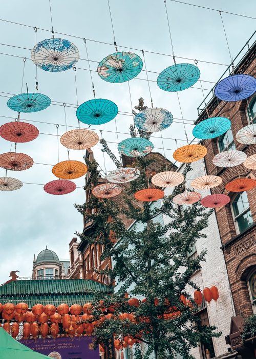 Colourful umbrellas above the shops and restaurants in Chinatown on your weekend in London with red lanterns behind