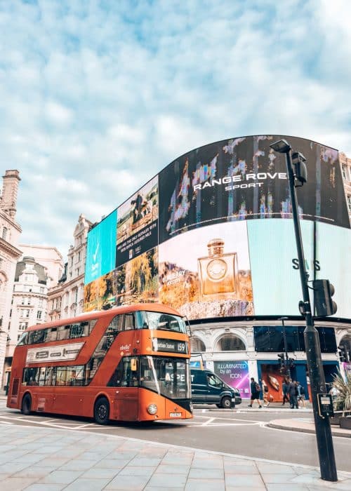 The large billboards with adverts on Piccadilly Circus with a red bus in front of them, London