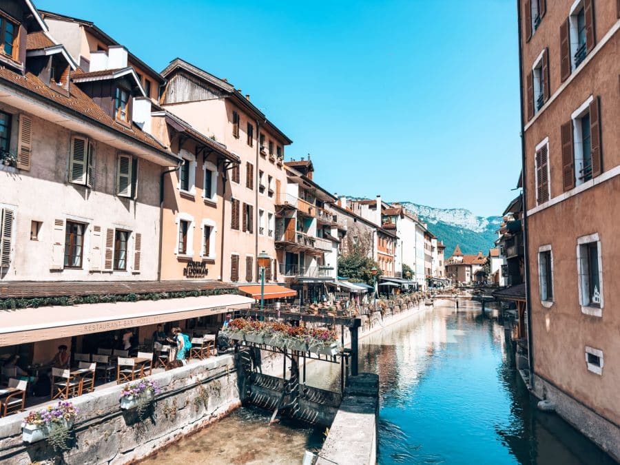 Restaurants overlooking the Thiou River leading to Lake Annecy with mountains in the background, France