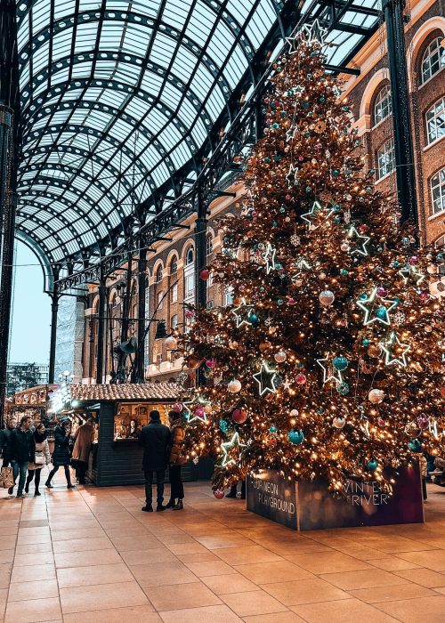 A large colourful Christmas tree with market stalls behind it at Christmas by the River, Christmas markets in London