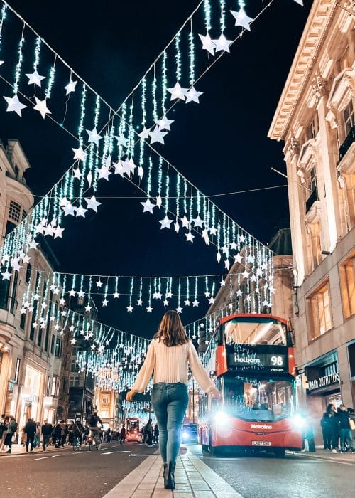 Helen walking down Oxford Street with some of the best Christmas lights in London. Twinkly stars strung between the buildings and a red bus driving up the road