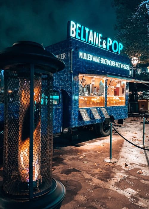 A wooden stall of mulled wine and warm festive drinks by a fire at Southbank Centre Winter Market in London at Christmas