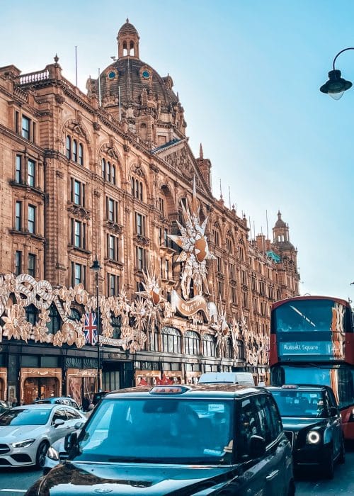 The front of Harrods with its gold Christian Dior decorations and a red bus driving outside is an iconic London at Christmas scene