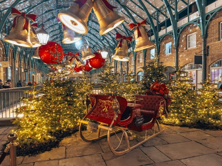 Santa's sleigh in front of several Christmas trees underneath giant gold bells and red bows, Covent Garden at Christmas, best Christmas decorations in London 2024