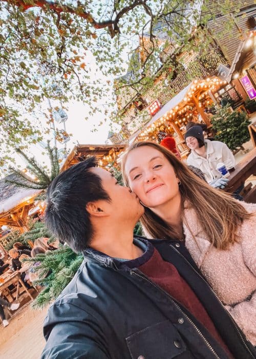 Andy kissing Helen's cheek in Winter Wonderland surrounded by Christmas trees and wooden cabins, London