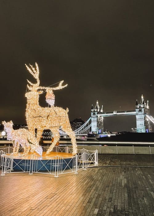 Sparkling reindeer lit up in front of Tower Bridge also lit up at night is one of the most iconic London at Christmas scenes