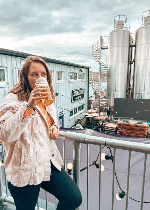 Helen drinking a beer on the terrace of Signature Brew overlooking the beer garden amongst the big vats, Walthamstow, London