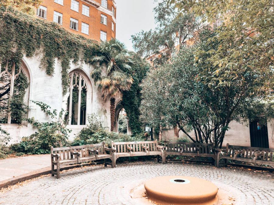 Benches in a circle in front of blackened ruined walls with vines creeping down them, St Dunstan in the East Church Gardens, London