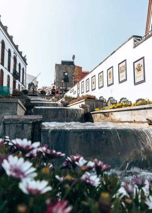 A 30-metre waterfall flowing down Paseo de Gran Canaria lined with colourful flowerbeds in Firgas, one of the best places to visit in Gran Canaria, Spain