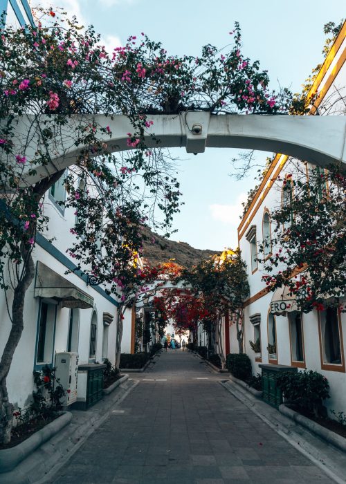 A white archway across quaint narrow streets lined with white-washed houses donned with beautiful colourful flowers in Puerto de Mogan, Gran Canaria, Spain
