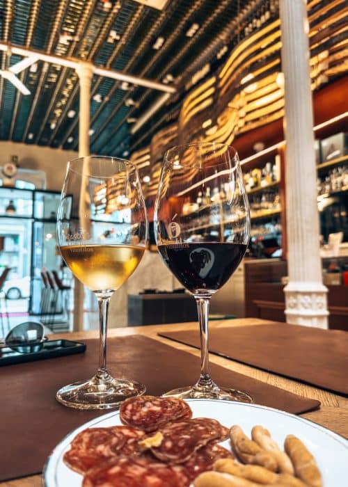 Glasses of red and white wine with a plate of cured meats in Vinófilos Triana, with hundreds of bottles of wine on the walls and ceilings, Las Palmas, Gran Canaria