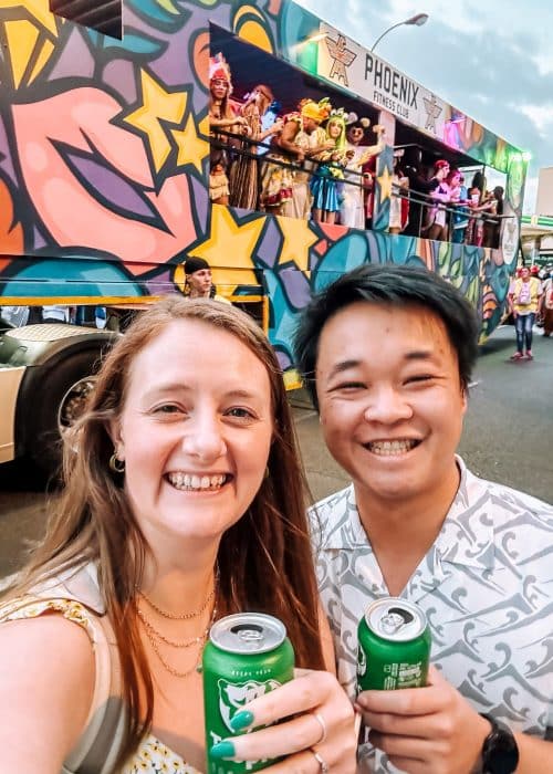 Helen and Andy drinking beer in front of a vibrantly decorated truck at the Las Palmas Carnival 2024, Gran Canaria, Spain