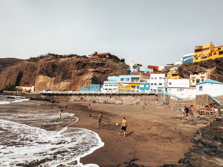 A black sand beach with brightly coloured houses climbing up the cliffs looking over the ocean, Sardina del Norte, Galdar, Gran Canaria