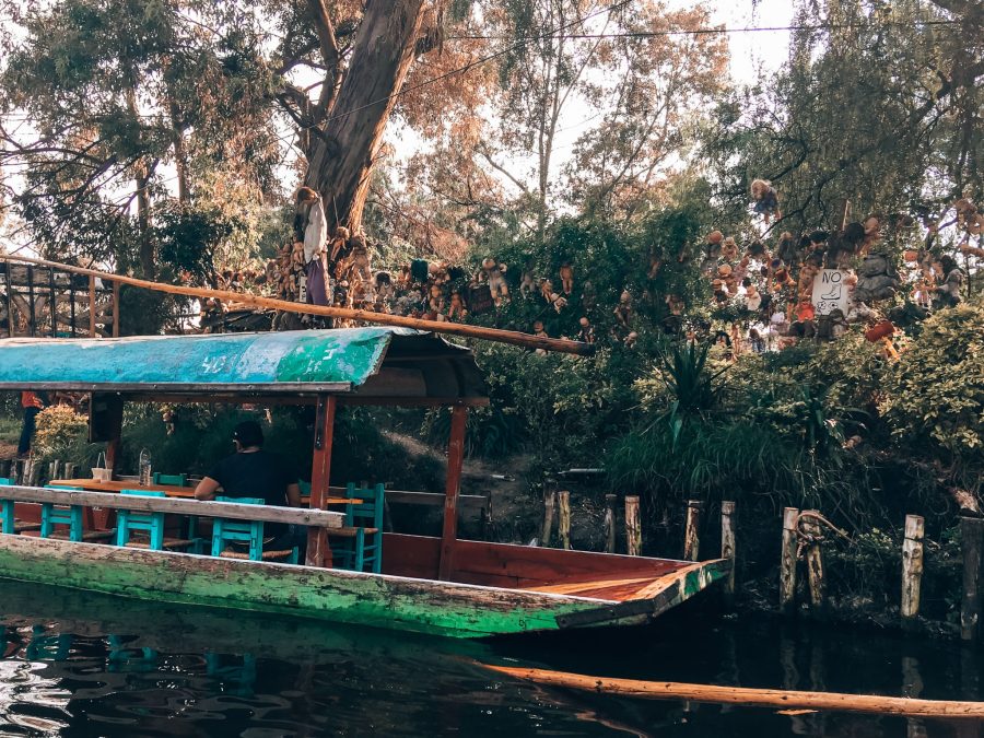 A colourful trajinera in front of a number of dolls hanging from trees at Isla de las Munecas, Floating Gardens of Xochimilco, Mexico City