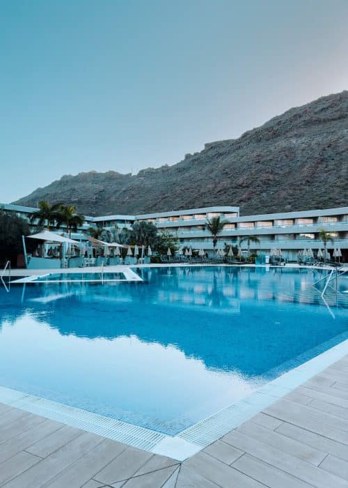 A swimming pool with hotel rooms behind it built into the rock behind at the Radisson Blu Puerto de Mogan, Canary Islands, Gran Canaria, Spain