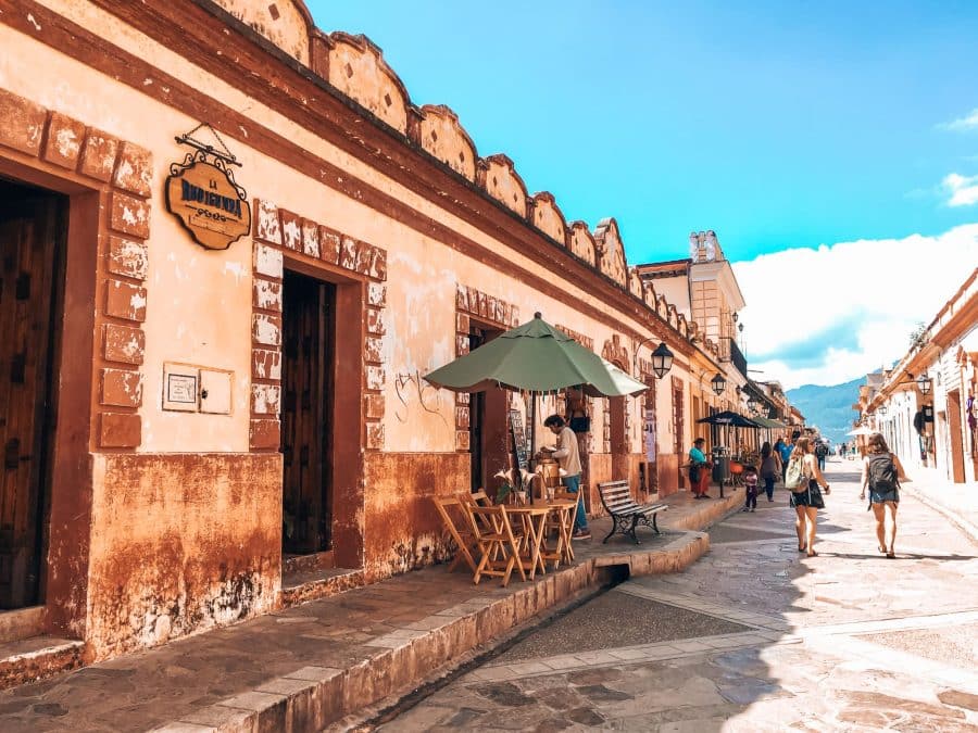 A pedestrianised colourful colonial street in San Cristobal de las Casas with tables and chairs from the restaurants on the street