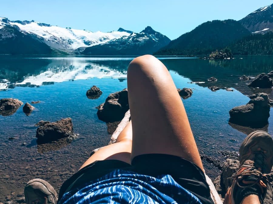 Helen lying on a log looking out across the tranquil Garibaldi Lake to the imposing Sphinx Glacier in Garibaldi Provincial Park, Canada