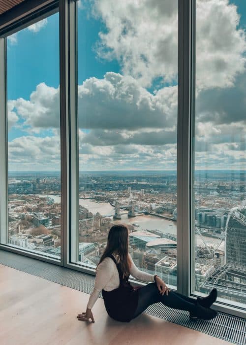 Helen looking out of floor-to-ceiling glass windows with Tower Bridge and the River Thames in the background, The Lookout London, Free viewing platforms in London