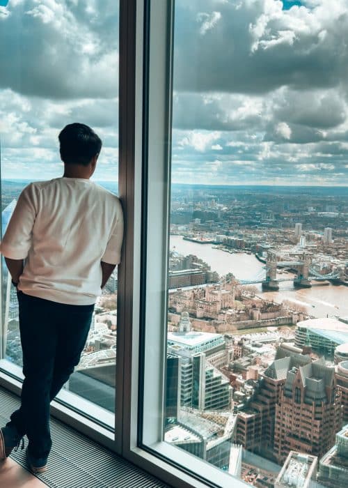 Andy looking out of floor-to-ceiling glass windows to the Tower of London and Tower Bridge, The Lookout at 8 Bishopsgate, best viewpoints in London