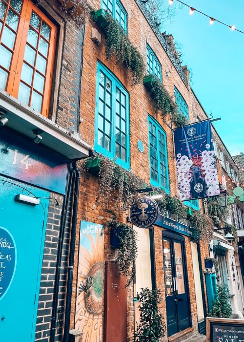 A narrow alley with buildings with bright blue and orange window frames in Neal's Yard, one of the most colourful places in London