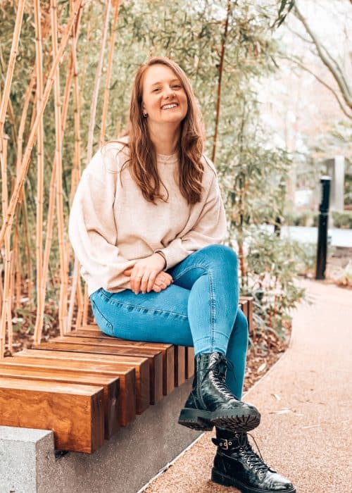 Helen sat on a bench surrounded by greenery and plants at the Crossrail Place Roof Garden in Canary Wharf, best free views of London