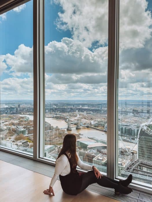Helen sat on the floor by huge glass windows looking out to Tower Bridge from The Lookout, London