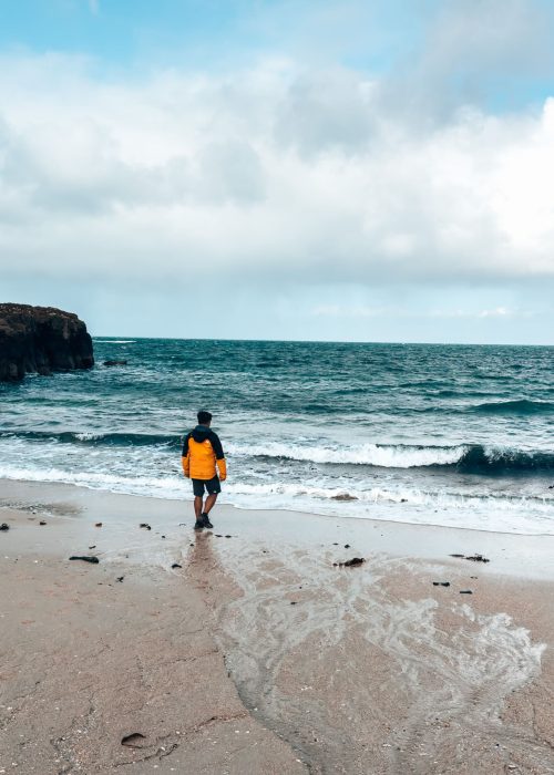 Andy stood in front of the turquoise ocean on white sand at Langamull Beach, places to visit on the Isle of Mull, Scotland