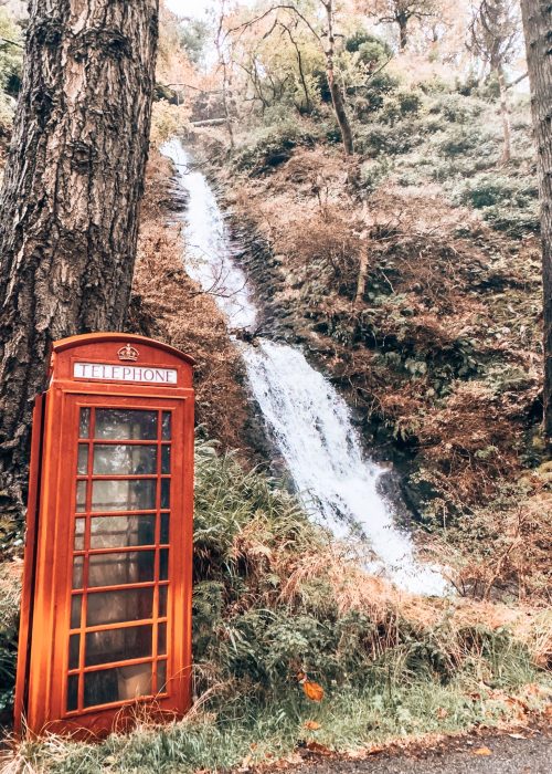 A red telephone box in front of a waterfall at Carsaig, Isle of Mull, Scotland