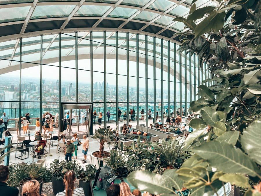 Lots of plants and groups of people in front of floor-to-ceiling glass windows at the Sky Garden, Free Viewpoint in London